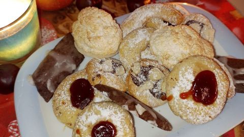 Ein Teller mit verschiedenen Plätzchen, umgeben von Äpfeln und Kerzen, schafft eine gemütliche Backatmosphäre.