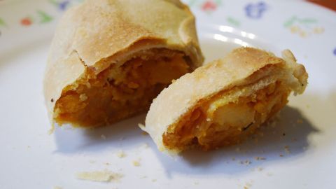 Ein Kürbisstrudel liegt auf einem Teller, auf dem eine Hälfte aufgeschnitten ist und die Füllung sichtbar macht.
