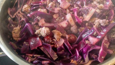 Eine bunte Rotkohlpfanne mit zartem Hackfleisch kocht dampfend in einer Pfanne auf einem hellen Tisch.