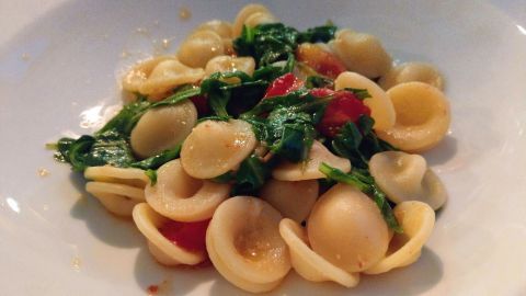 Orecchiette liegen in einem weißen Teller und sind mit Rucola und kleinen Tomaten vermischt.
