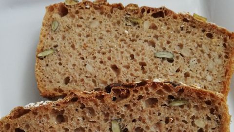 Zwei Scheiben gesundes Vollkornbrot liegen auf einem weißen Teller, mit sichtbaren Körnern und einer rustikalen Kruste.