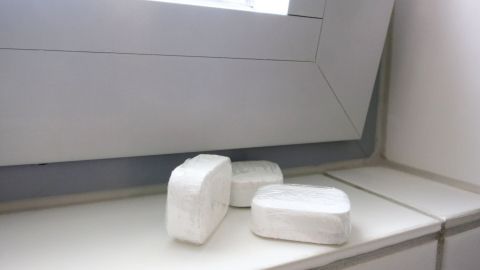 Drei Spülmaschinentabs liegen auf einer weißen Fensterbank neben einem sauberen Fensterrahmen.