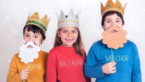 Drei Kinder in bunten Shirts und Kappen stellen die Heiligen Drei Könige dar, lächeln und halten Requisiten in der Hand.