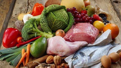 Frisches Gemüse, Obst, Fleisch und Fisch liegen auf einem rustikalen Holztisch, ideal für die Paleo-Diät.
