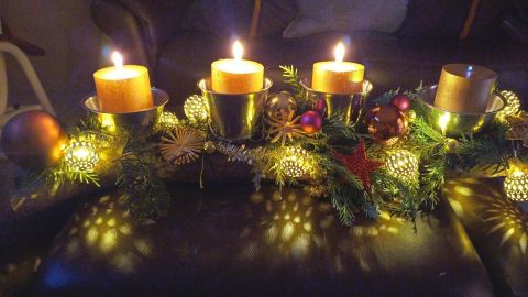 Ein Adventskranz mit brennenden Kerzen strahlt festliche Atmosphäre auf einem dunklen, gemütlichen Sofa aus.