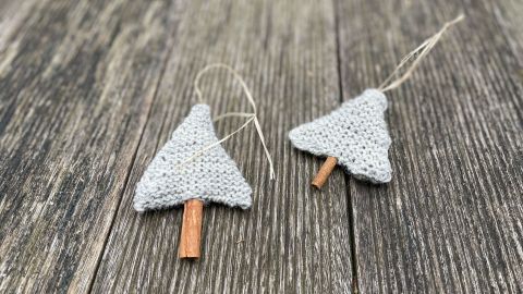 Gestrickte Weihnachtbäumchen liegen auf einer rustikalen Holzoberfläche und zeigen zwei dekorative, kleine Tannenbäume.