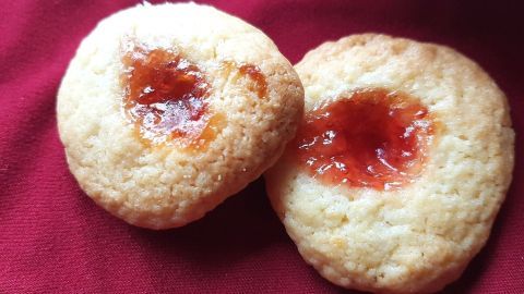 Zwei einfache Weihnachtsplätzchen mit einer glänzenden Marmeladenfüllung liegen auf einem roten Tuch.