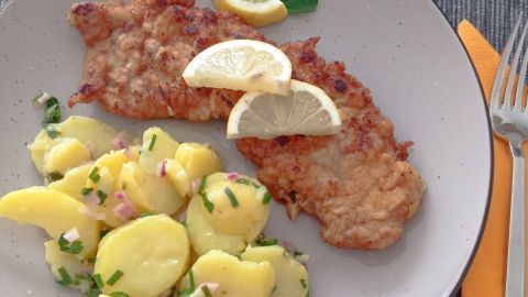 Ein goldbraun gebratenes Wiener Schnitzel liegt neben einem frischen Erdäpfel-Salat, garniert mit Zitrone und Petersilie.