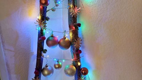 Eine dekorative Leiter ist mit bunten Lichtern und Weihnachtskugeln geschmückt und strahlt festliche Stimmung aus.