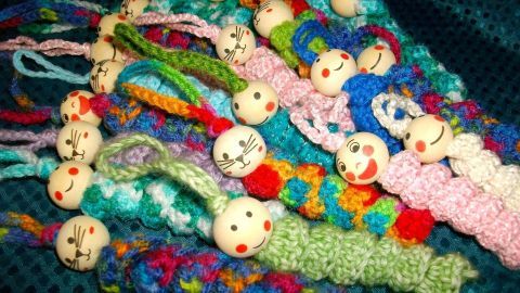 Bunte, gehäkelte Sorgenwürmchen mit fröhlichen Gesichtern liegen auf einem blauen Stoff, bereit zum Spielen oder Verschenken.