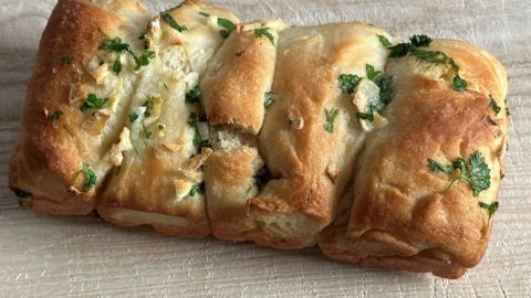 Goldbraunes Knoblauchbrot mit Käse liegt auf einem Holzbrett und zeigt die Schnittflächen mit Kräutern.