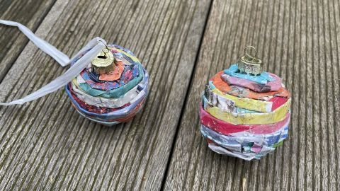 Bunte Weihnachtskugeln aus Papier liegen auf einem Holztisch. Sie sind spiralig gewickelt und verziert.