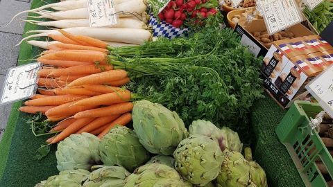 Frische Artischocken liegen auf einem Marktstand, umgeben von buntem Gemüse, das ansprechend präsentiert wird.