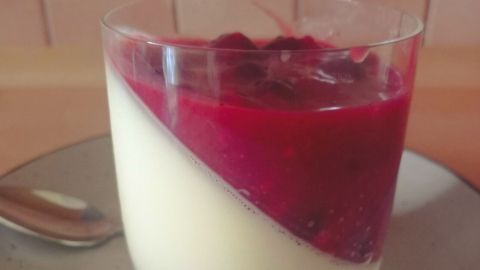 Eine cremige Panna Cotta liegt in einem Glas, gekrönt von fruchtigem Beerenkompott auf einem Teller.