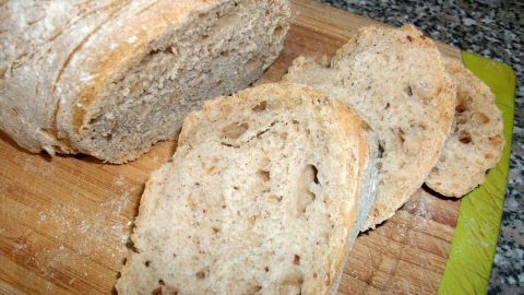 Ein frisches Brot mit Mandelmus liegt auf einem Holzbrett, einige Scheiben sind geschnitten und zeigen die innere Textur.
