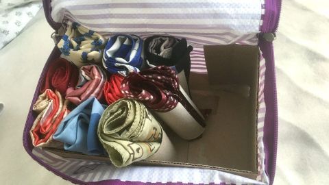 Mit Klopapierrollen kannst du ganz einfach Ordnung schaffen und deine Kleidungsstücke übersichtlich aufbewahren. Ordentlich gerollte Halstücher sind in einer gepunkteten Tasche verstaut, die auf einem Bett liegt.