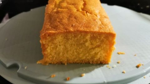 Ein goldbrauner Zitronenkuchen liegt auf einem Teller, frisch geschnitten, mit saftigem, weichem Inneren sichtbar.