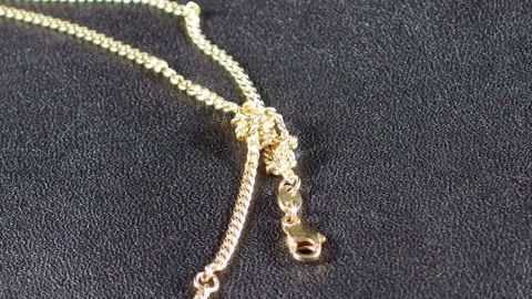 So kann man Knoten aus Schmuckketten sehr gut lösen. Ein goldfarbenes Schmuckkettchen mit einem Knoten liegt auf einem dunklen Untergrund, während es gelöst wird.