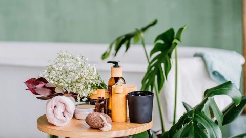 Ein Holztisch präsentiert Wellness-Produkte, Handtücher und frische Blumen in einem entspannenden Badezimmer mit Pflanzen.