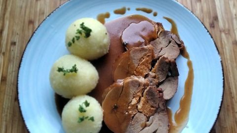 Putenrollbraten liegt in reichhaltiger Schwarzbiersoße auf einem Teller, begleitet von knusprigen Kartoffelknödeln.