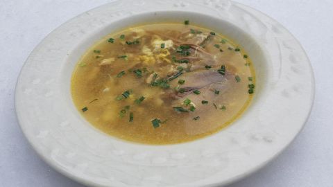Eine Schüssel mit klarem Suppenbrühe, gefüllt mit Suppenhuhn und frischen Kräutern, steht auf einer frostigen Unterlage.
