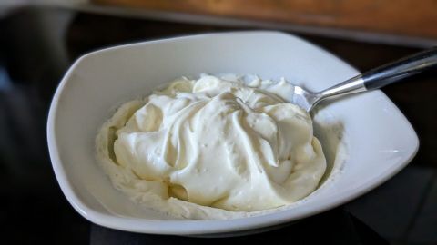 Eine Schüssel mit cremiger Crème fraîche steht auf einem Tisch, während ein Löffel bereitliegt, um sie zu servieren.