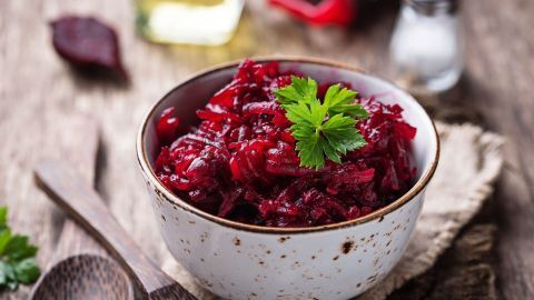 Eine Schüssel mit rot gefärbtem Rote Bete Salat, garniert mit frischer Petersilie, steht auf einem rustikalen Holztisch.