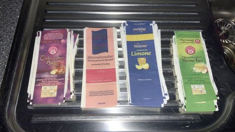 Notizzettel aus Teebeutelhüllen liegen ordentlich nebeneinander auf einem Waschbeckenrost in einer modernen Küche.