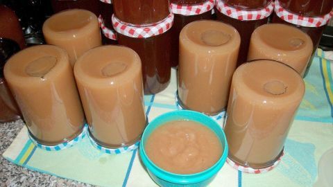 Sechs Gläser mit köstlichem Birnen-Apfelmus stehen auf einem Tisch, neben einer kleinen Schüssel mit frischem Mus.