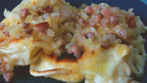 Käsespätzle sind auf einem Teller mit goldbraunem Käse und angebratenen Zwiebeln, bereit zum Genießen.