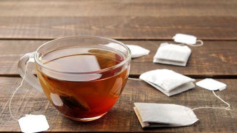 Eine transparente Tasse mit Tee steht auf einem Holztisch, umgeben von benutzten Teebeuteln, die zur Wiederverwendung anregen.