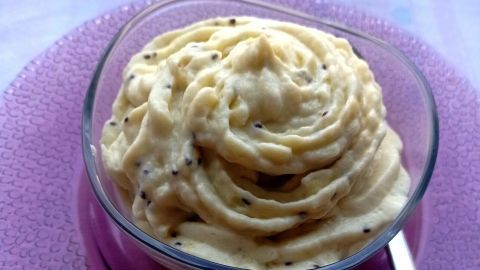 Cremige Kiwi-Sahne-Creme wird in einer Schüssel serviert, umgeben von einem lila Teller auf einem hellen Tisch.