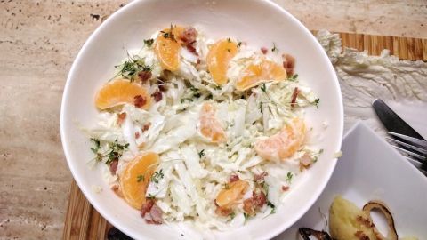 Ein frisch zubereiteter Chinakohlsalat mit Joghurt-Dressing, garniert mit Orangenstücken und Kräutern, in einer Schüssel.