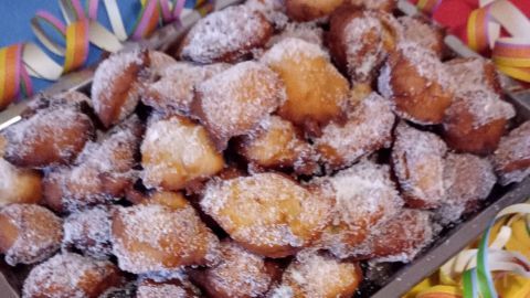 Ein Blech mit Quarkbällchen, die mit Puderzucker bestäubt sind, liegt auf einem bunten Tisch, umgeben von Konfetti.