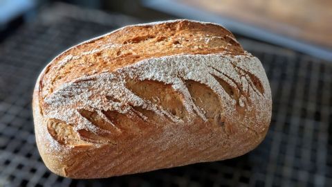 Ein frisch gebackenes Dinkel-Weizen-Roggenbrot liegt auf einem Gitter, während die Kruste goldbraun und knusprig aussieht.