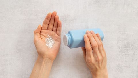 Eine Hand hält eine blaue Flasche, während Puder in die andere Hand gestreut wird, um Stielwarzen zu entfernen.