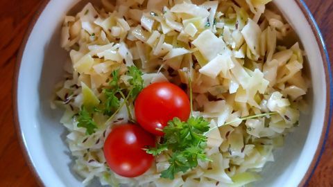 Weißkrautsalat mit frischen Tomaten und Kräutern in einer Schüssel, serviert auf einem Holztisch.