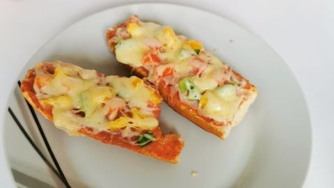 Zwei belegte Pizzabaguettes auf einem Teller, frisch überbacken mit Käse und Gemüse, bereit zum Servieren.