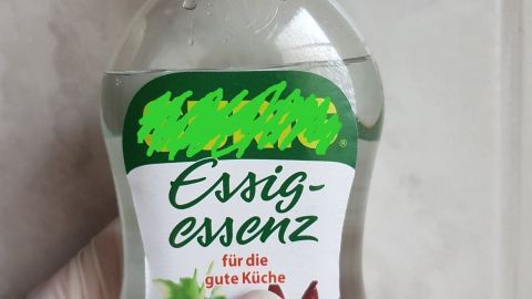 Eine Hand hält eine Flasche Essig-Essenz, die für die Küche mit Gemüseillustrationen auf dem Etikett beschrieben wird.