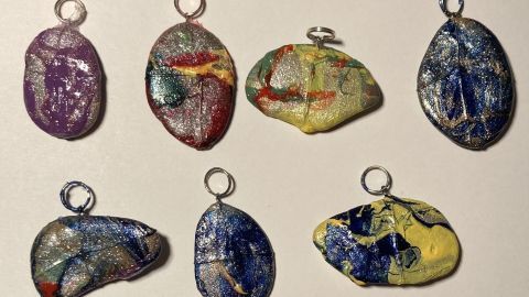 Bunte, individuell gestaltete Schlüsselanhänger aus Nagellackresten liegen auf einer hellen Fläche.