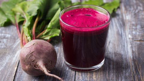 Ein Glas Rote Bete Saft steht auf einem Holzuntergrund, daneben liegt eine frische Rote Bete, umgeben von Blättern.