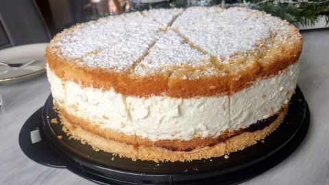 Eine Käsesahnetorte mit knusprigem Boden steht auf einem schwarzen Tortenboden, mit Puderzucker bestäubt, in heller Umgebung.