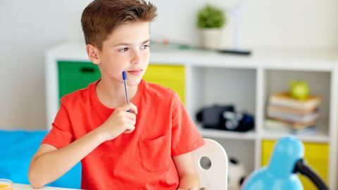Ein Junge in einem roten Shirt denkt nach, während er einen Stift in der Hand hält, umgeben von bunten Möbeln.