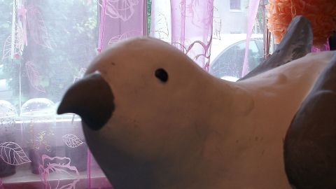 Ein Keramikvogel liegt vor einem Fenster, während Tageslicht durch den pinken Vorhang strömt und den Raum erhellt.