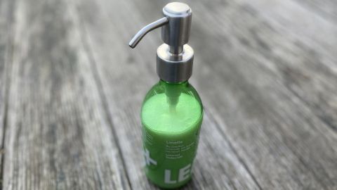 Eine grüne Flüssigseife steht auf einem Holzuntergrund und wartet darauf, durch den Pumpmechanismus entnommen zu werden.