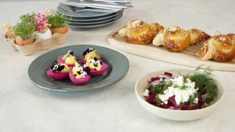 Bunte gefüllte Eier auf einem Teller, umgeben von frischen Brötchen und einem Salat, schaffen eine einladende Osterbrunch-Tafel.