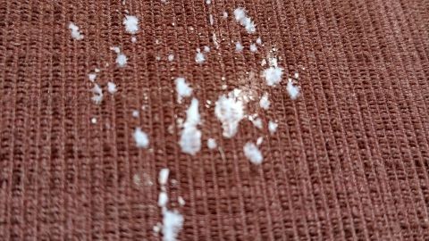 Auf einem braunen Stoff sind weiße Flecken zu sehen, die von Kerzenwachs stammen. Sie warten darauf, entfernt zu werden.