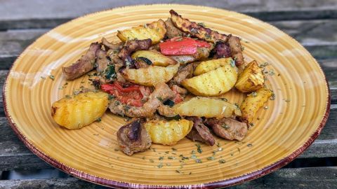 Eine bunte Gemüsepfanne mit knusprigem Schweinefilet liegt auf einem gelben Teller, umgeben von Holzuntergrund.