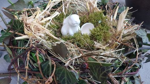 Ein festlich dekoriertes Osternest aus Zweigen, Heu und Moos, in der Mitte sitzt ein kleiner weißer Hase.