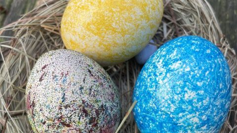 Bunte Ostereier liegen in einem Nest aus Heu, während sie im Freien auf einem Holztisch präsentiert werden.